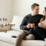 A relaxed couple sitting on a cream sofa holding warm mugs, sharing a quiet moment to reconnect and start managing post-holiday burnout as a couple after Thanksgiving.